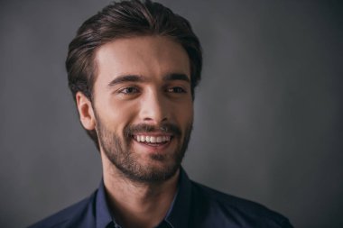 Yakışıklı emin işadamı kıl, koyu mavi gömlek ile uzağa bakarak ve, gri arka plan üzerinde gülümseyen