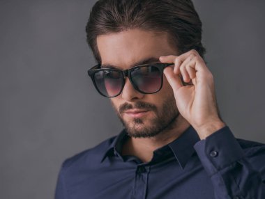 Koyu mavi gömlek ve güneş gözlüklü, gri arka plan üzerinde kıl ile yakışıklı emin işadamı