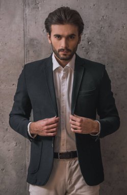 Yakışıklı emin işadamı ile kıl, takım elbise, gri arka plan üzerinde kamera bakıyor