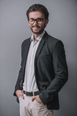 Takım, kıl ile şık işadamı kameraya bakıyor ve gri arka plan üzerinde cepler içinde ayakta, gülümseyen eller