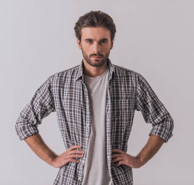 Rahat kıyafetler içinde sakallı yakışıklı açık renkli akimbo ayakta iken kameraya bakıyor