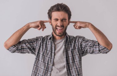 Yakışıklı sakallı adam rahat kıyafetler içinde onun kulaklarını kapatma ve çığlık, açık renkli