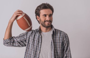 Yakışıklı sakallı adam rahat kıyafetler içinde bir futbol topu uzağa bakarak ve gülümseyen, açık renkli tutuyor