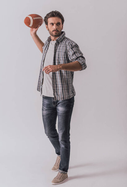 Full length portrait of handsome bearded man in casual clothes throwing a football ball, on light background