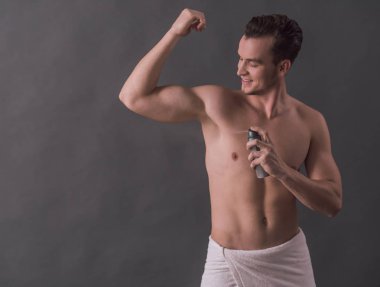 Yakışıklı genç çıplak gövde ile terlemeyi önleyici kullanarak ve gri arka plan üzerinde gülümseyen
