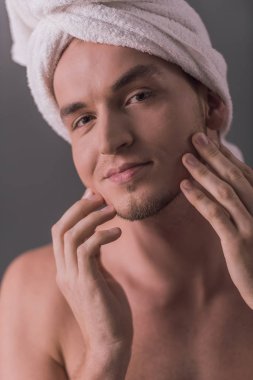 Yakışıklı genç adam çıplak gövde ve havlu kafasında yüzünü dokunaklı ve gri arka plan üzerinde gülümseyen