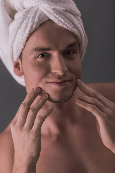 英俊的年轻男子裸露躯干和毛巾在他的头上触摸他的脸和微笑 在灰色背景 — 图库照片