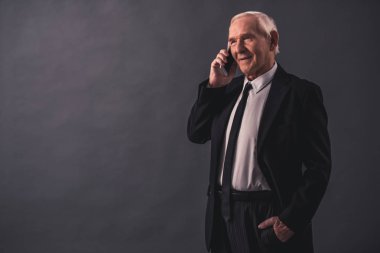 Takım elbiseli yakışıklı eski işadamı cep telefonda konuşurken ve gri arka plan üzerinde gülümseyen