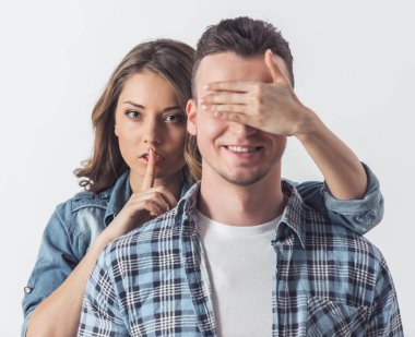 Güzel genç bir çift beyaz arka plan üzerinde. Kız sevgilisinin gözleri, sessizlik işaret gösteren kapsayan ve kameraya baktığımızda, her ikisi de gülüyorsun