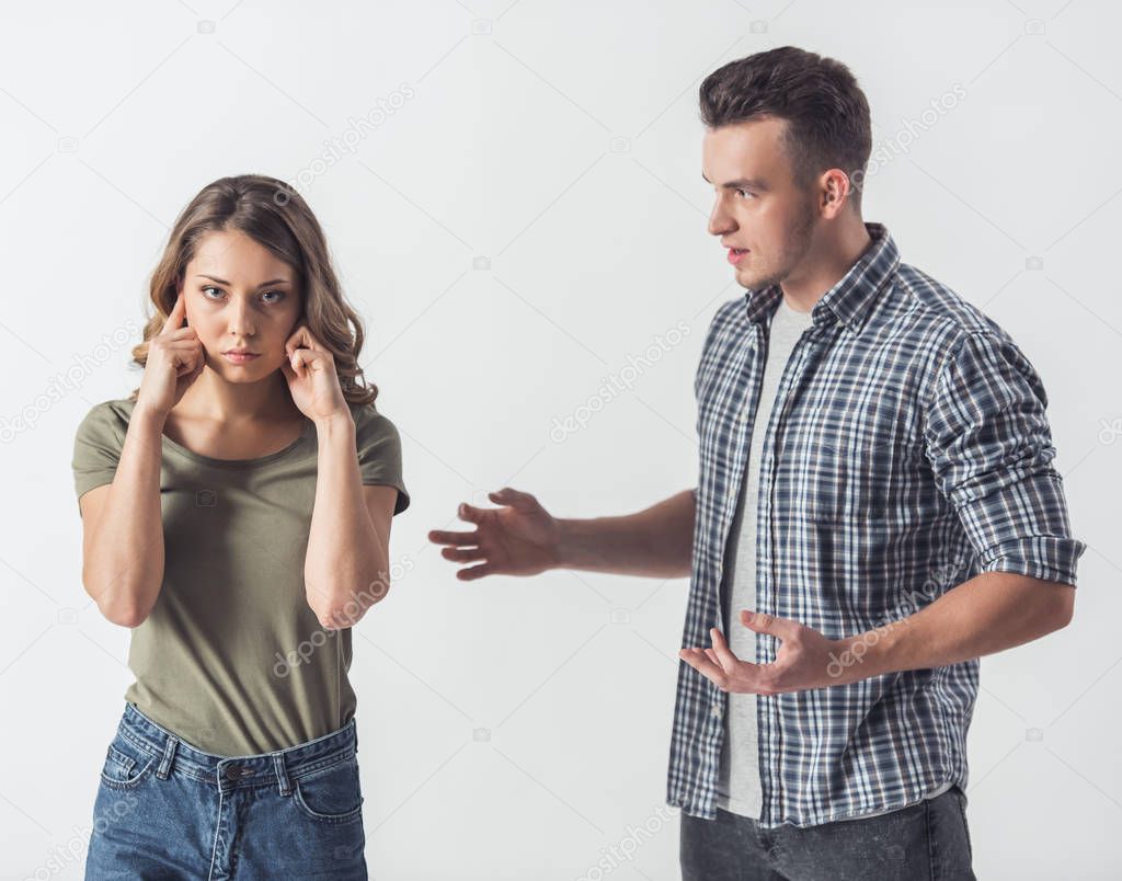 Young couple having problems. Girl is covering her ears at her boyfriend is talking to her, isolated on white