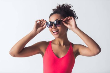 Parlak pembe mayo ve güneş gözlüklü güzel Afro-Amerikan kız kameraya bakıyor ve gülümsüyor, üzerinde beyaz izole