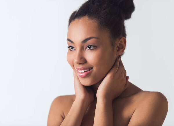 Beautiful Afro-American girl is touching her face and smiling, isolated on white