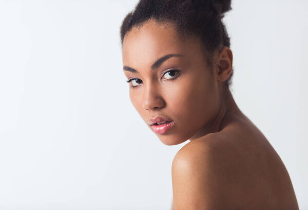 Beautiful Afro-American girl with bare shoulders is looking at camera, isolated on white