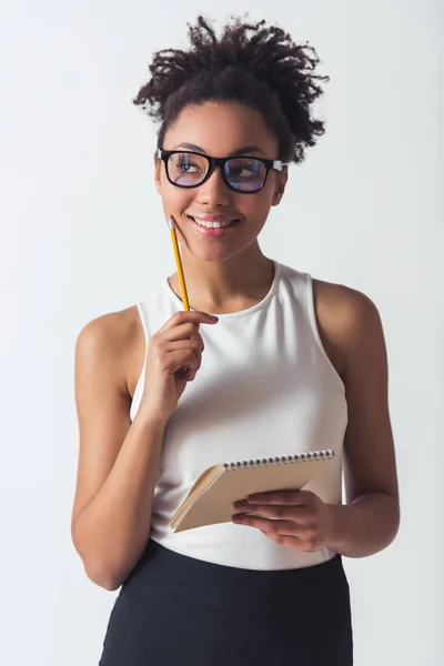 眼鏡でアフリカ系アメリカ人の美女は メモ帳を保持しているし 離れているし 笑みを浮かべて 鉛筆は 白で隔離 — ストック写真
