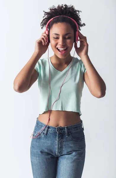 Stylish Afro-American girl in casual clothes and headphones is listening to music and smiling, isolated on white