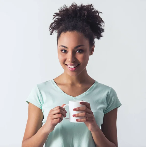 快活的黑人美国女孩在休闲衣服拿着一个杯子 看着相机和微笑 孤立的白色 — 图库照片