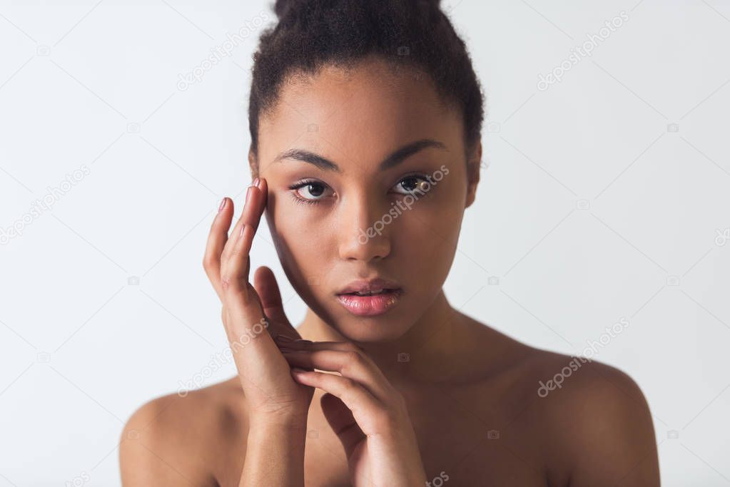 Beautiful Afro-American girl is touching her face and  looking at camera, isolated on white