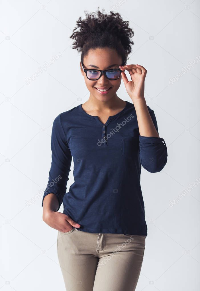 Beautiful Afro-American girl in casual clothes and eyeglasses is looking at camera and smiling, isolated on white