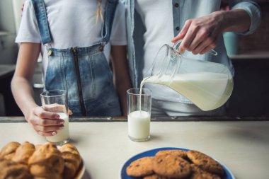 Anne ve kızı evde mutfakta rahat kıyafetler içinde görüntü kırpılmış, anne sütü döküyor