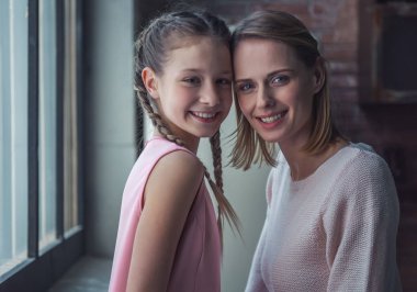 Anne ve kızı kameraya bakarak ve evde mutfakta dururken gülümseyen