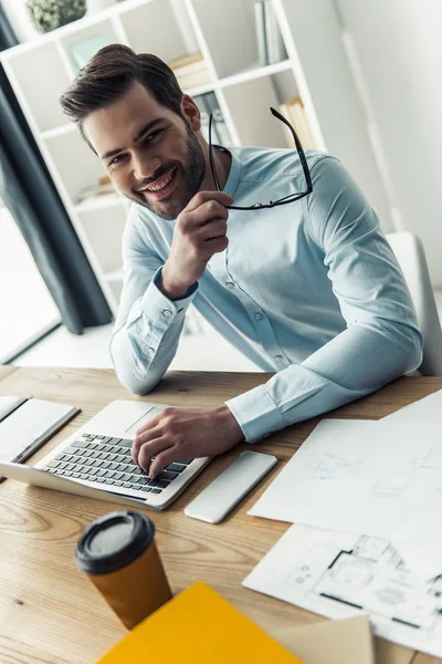 Hombre Negocios Guapo Está Sosteniendo Gafas Mirando Cámara Sonriendo Mientras — Foto de Stock