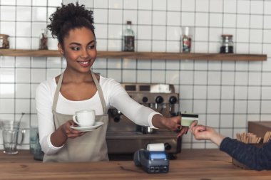 Güzel Afro Amerikan barista önlük bir istemciye, kredi kartı ve sayaç bar, dururken gülümseyerek veriyor