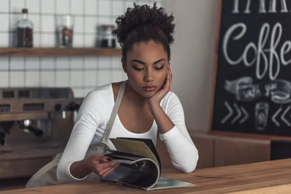 Schöne Afroamerikanische Gelangweilte Barista Schürze Liest Eine Zeitschrift Während Sie — Stockfoto