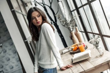 Güzel genç kız rahat kıyafetler içinde uzak evde ahşap masanın üzerine eğilerek arıyor