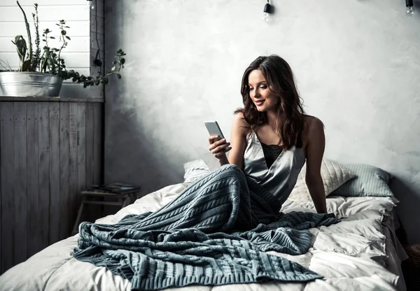 스마트폰 집에서 침대에 앉아있는 — 스톡 사진