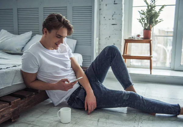 Jovem Bonito Roupas Casuais Está Usando Telefone Inteligente Sorrindo Enquanto — Fotografia de Stock