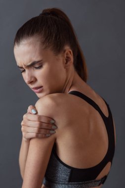 Güzel kızı spor giyim gri arka plan üzerinde omuz duygu acısını dokunuyor