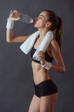 Spor giyim güzel kızı bir havlu ve içme suyu, gri arka plan üzerinde tutuyor