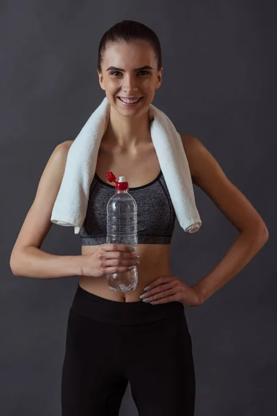 Piękna Dziewczyna Sportowej Trzyma Butelkę Wody Patrząc Kamery Uśmiechnięty Szarym — Zdjęcie stockowe