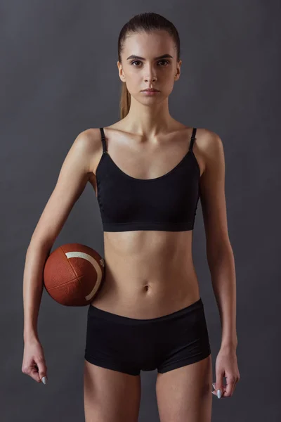 Piękna Dziewczyna Sportowej Trzyma Piłkę Futbolu Amerykańskiego Patrząc Kamery Szarym — Zdjęcie stockowe