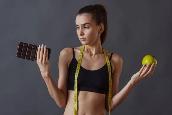 Schönes Mädchen Sportbekleidung Hält Einen Apfel Und Schokoriegel Auf Grauem — Stockfoto