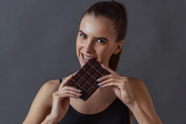 Beautiful Girl Sportswear Biting Chocolate Bar Looking Camera Gray Background — Stock Photo, Image
