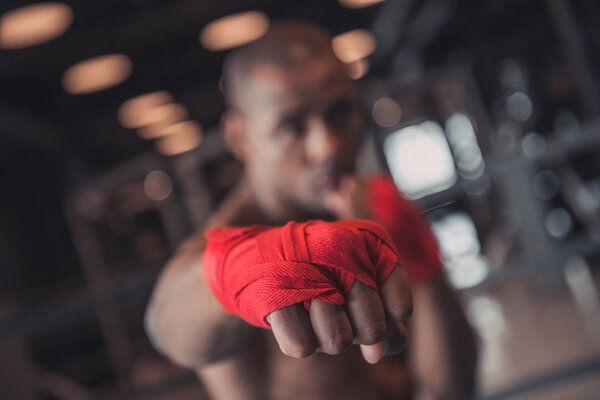 Afro American boxer, his hands wrapped in red bandage, is training in gym, hand in focus