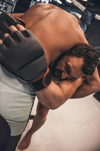 Two men in boxing gloves and shorts are fighting in cage using grappling technique