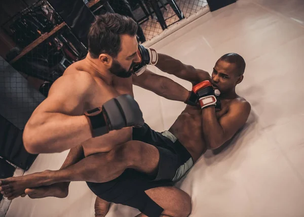 Two men in boxing gloves and shorts are fighting in cage