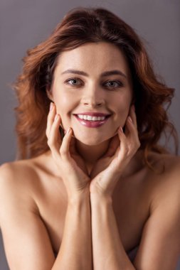 Gri bir arka plan ve bir gülümseme kameraya çıplak omuzlarına olan güzel bir kadın portresi