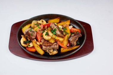 Beyaz arka planda et ve patatesli kızgın demir tava.