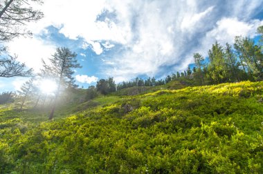 Dağlık arazi ve güneş ışınlarıyla mavi gökyüzü