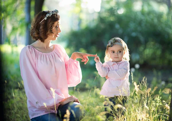 Mom and daughter are two years old sitting on the grass in the park, woman and child in nature
