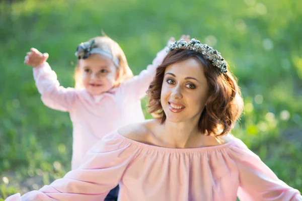 Mom and daughter are two years old sitting on the grass in the park, woman and child in nature