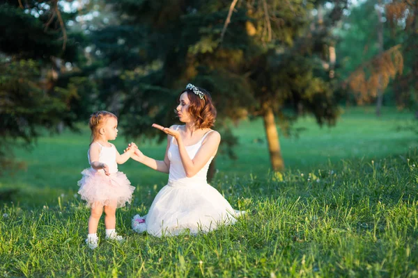 Mom and daughter are two years old sitting on the grass in the park, woman and child in nature