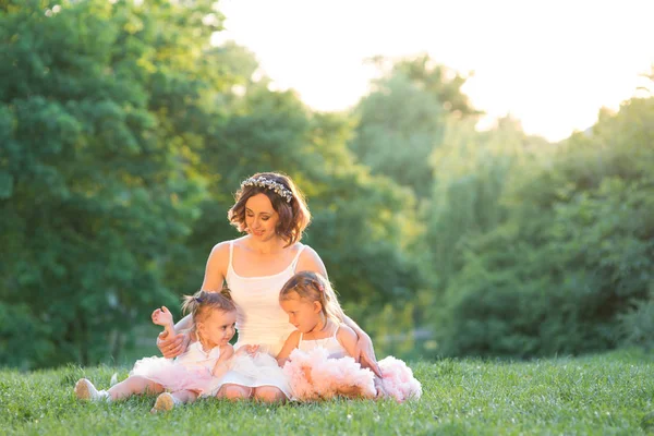 Mom and daughter are two years old and four years old sitting on the grass in the park, a woman and children in nature