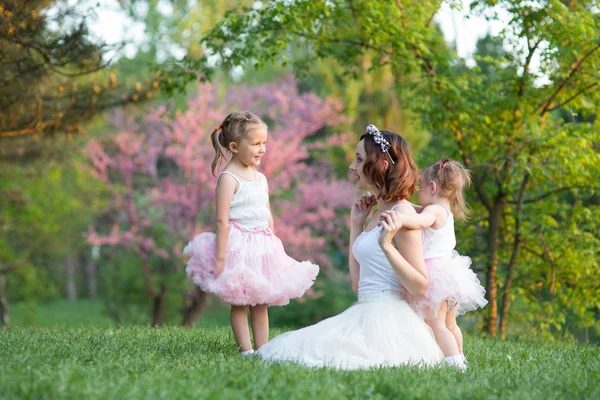 Mom and daughter are two years old and four years old sitting on the grass in the park, a woman and children in nature