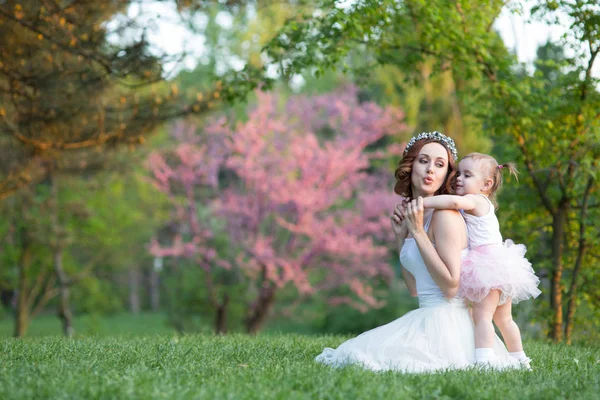 Mom and daughter are two years old sitting on the grass in the park, woman and child in nature