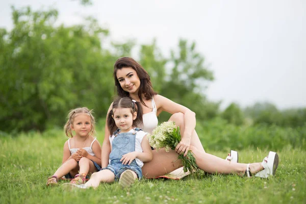 Mom and daughter on the grass in the park, a woman and children in nature