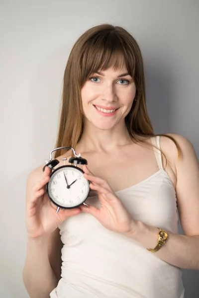 Young business woman with a clock in hands on gray background